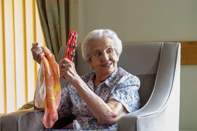 A care home resident smiling while holding aloft a coloured scarf and tambourine.