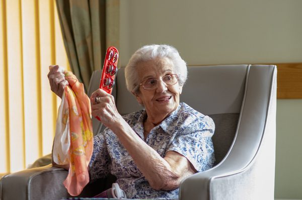 A care home resident smiling while holding aloft a coloured scarf and tambourine.