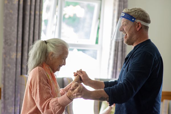 A new adventures dancer and a care home resident laughing as they hold hands to dance.