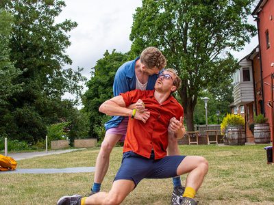 Two dancers perform together. One holds the other who leans back against him. An intense look holds between them.