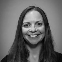 Black and white headshot of a woman with long dark hair smiling to camera.