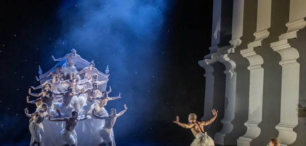 A flock of swans are posed with their arms out to imitate wings on the Prince’s bed. The Prince Is sat on the floor in fear, and the Swan is taking an aggressive stance and defending him.