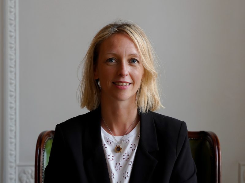 Imogen is seated, she is a white woman with blonde shoulder length hair, she is smiling.