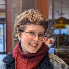 Julia has short fair hair, is smiling wearing a red scarf and glasses