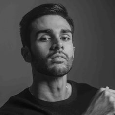 A mixed-race Asian-British man in his mid 20s with slicked back short black hair, looking towards the camera