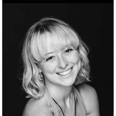 A woman in her early 20s, smiling to the camera. She is wearing two necklaces and earrings and has short blonde wavy hair with a fringe.
