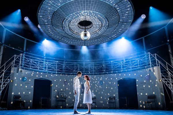 Male and female in white stand under a disco ball looking into each other's eyes