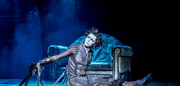 Edward sits alone in the old house. He sits on the floor with his hands behind him. His scissors prop him up.