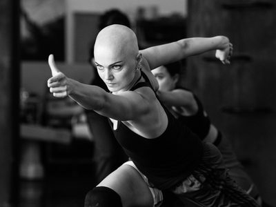 Rehearsal image of a dancer lunging forward, their arms outstretched and an intense expression on their face