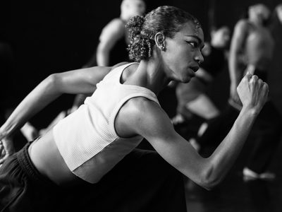 Rehearsal image of a dancer lunging forward with their arms in an athletic running position