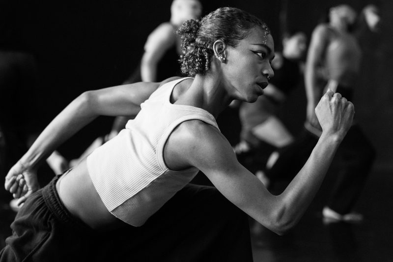 Rehearsal image of a dancer lunging forward with their arms in an athletic running position