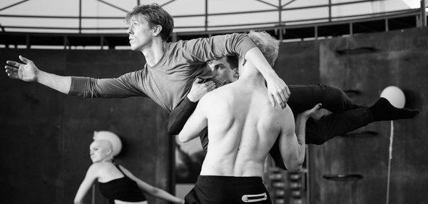 Rehearsal image of 2 dancers lifting another dancer as they reach forward with a longing gaze